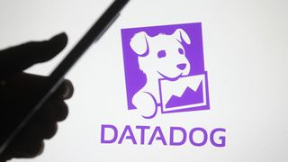 A person holding a smartphone in front of the Datadog logo