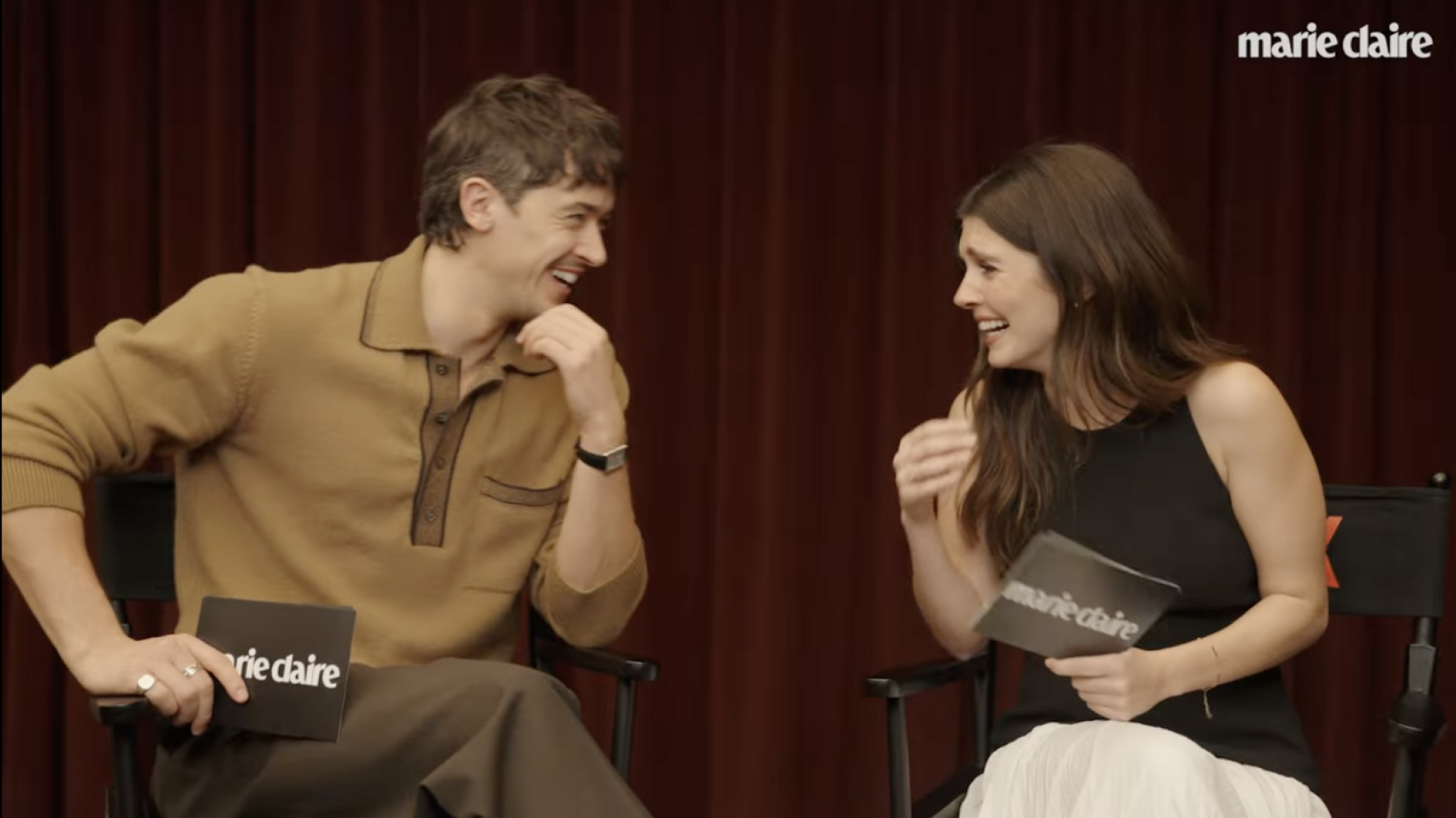 tom blyth rests his chin on his hand while making emily bader laugh as they film the marie claire trivia game how well do you know your costar