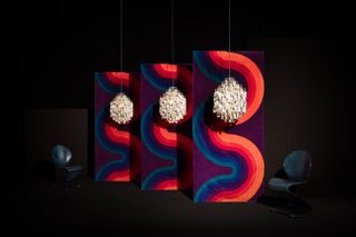 A dark room with a colourful background featuring a sinuous pattern, serving as the backdrop for Verner Panton chandeliers