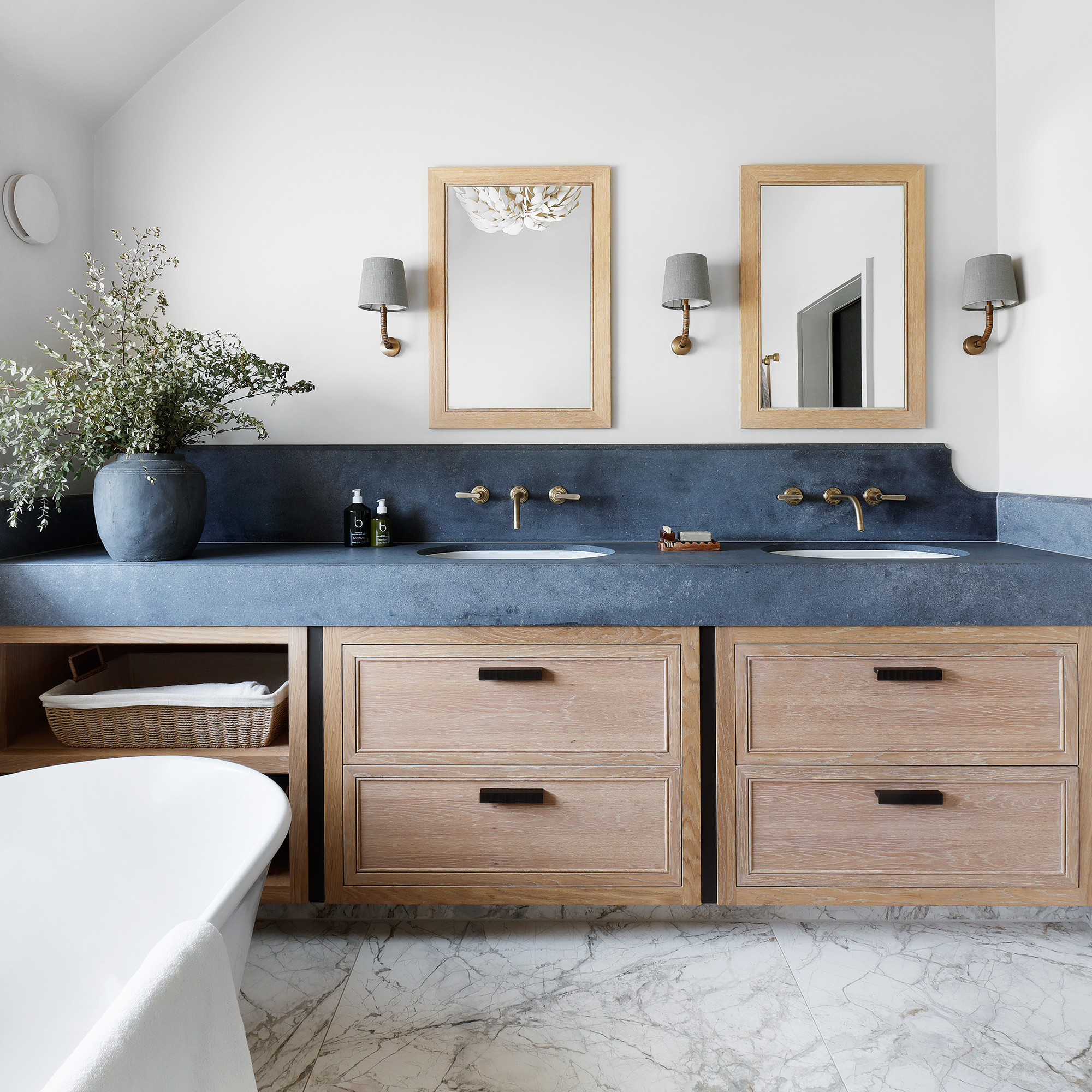 a neutral bathroom with twin washbasins set into a stylish wooden storage unit and concrete-coloured quartz surface, with matching mirrors and wall lights