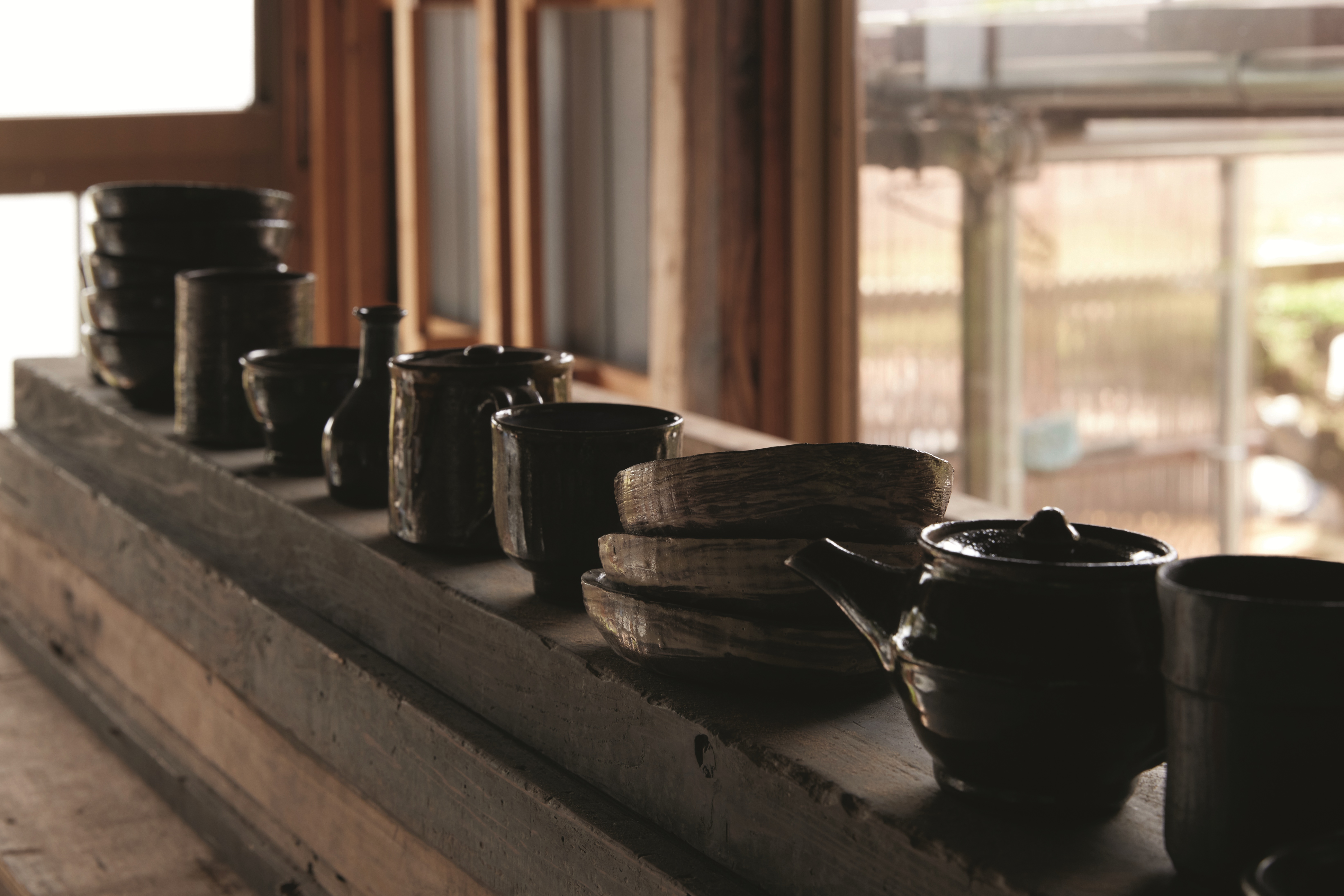 A series of ceramic tableware sits atop a wooden shelf.