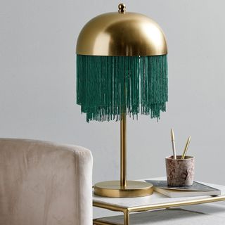golden fringed table lamp with grey wall