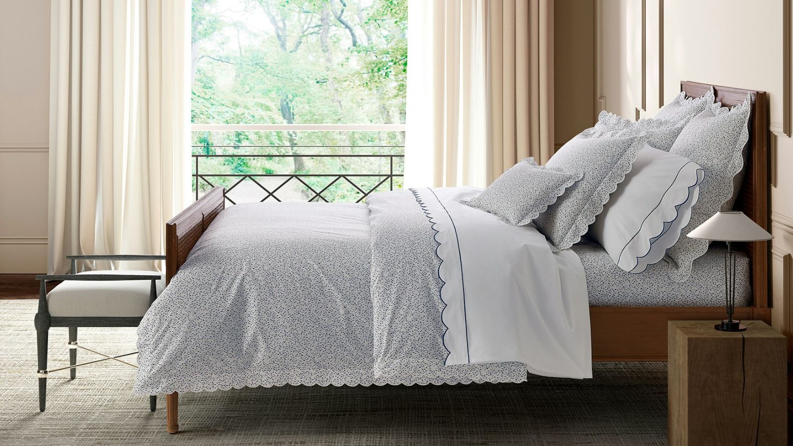 Neutral, modern bedroom with wooden bedframe, blue and white bedding, cream curtains and rug, wooden bed-side table with lamp, stool at the end of the bed