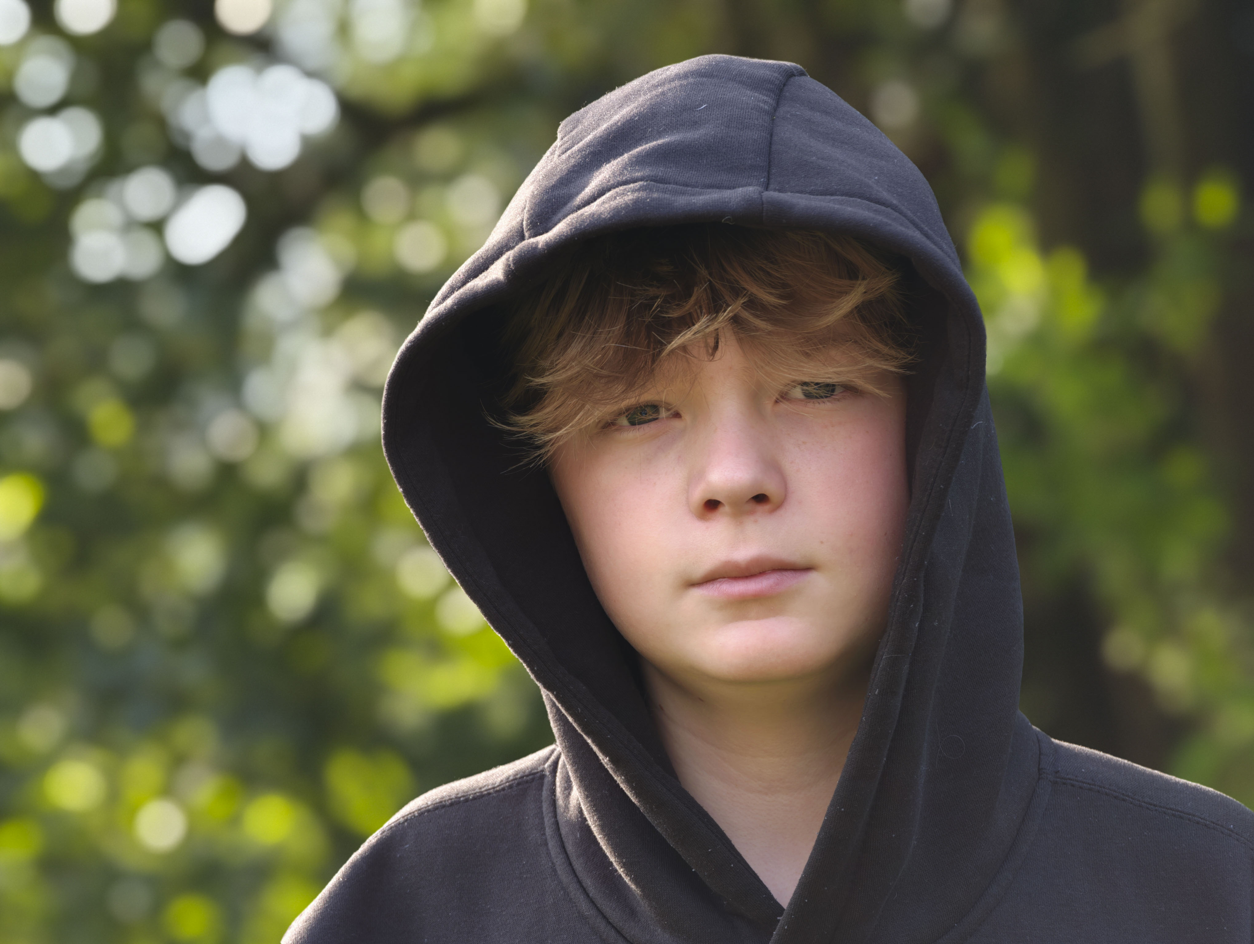 portrait of a boy in a hoodie with a dappled background light