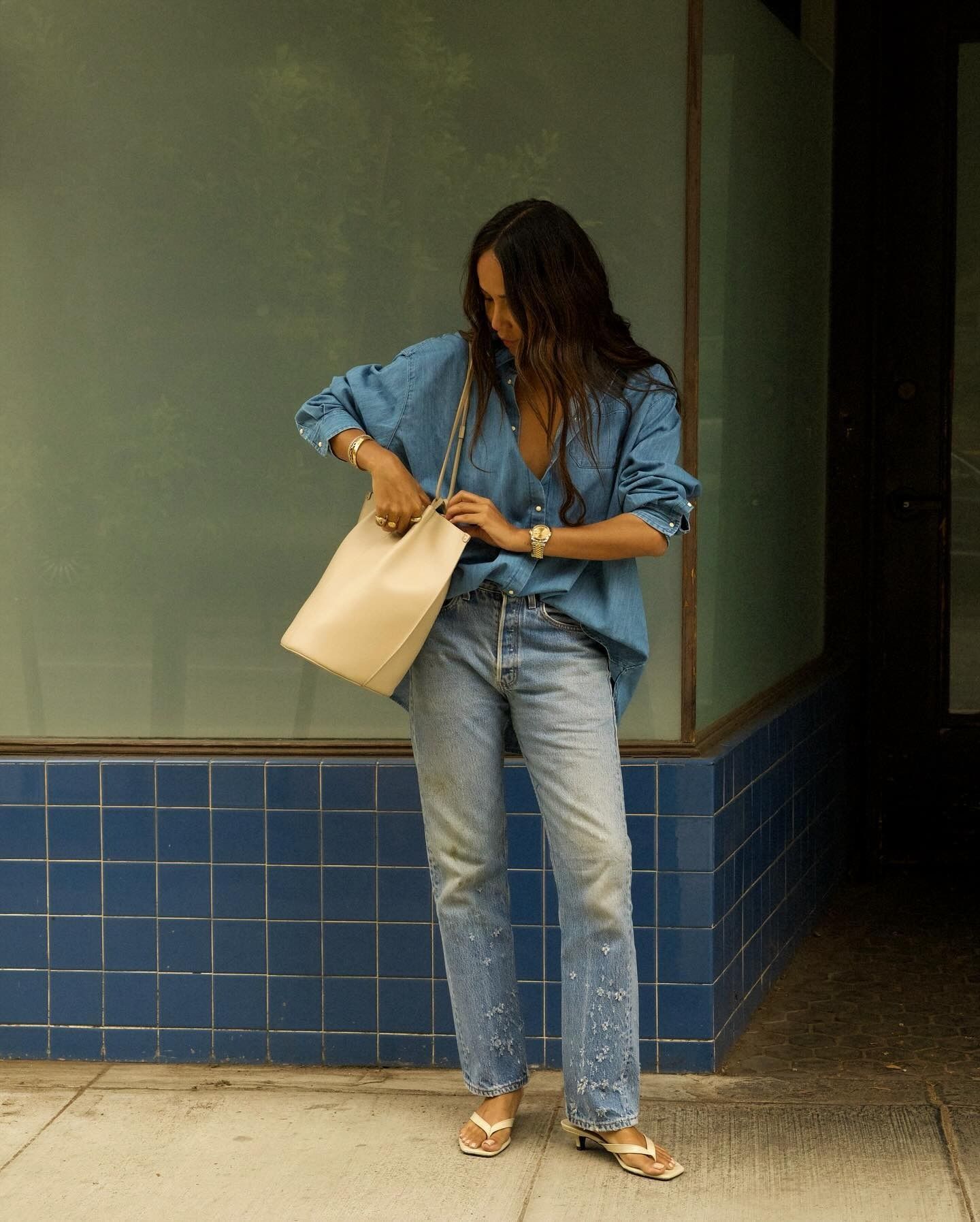 Influencer stand outside wearing distressed jeans with an oversized denim shirt and kitten heels flip-flops.