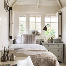 Small bedroom with pale cream walls, single bed with brown bedding, framed pictures on the walls and wooden vaulted ceiling