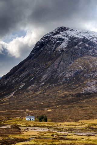 Wide angle view of small white cottage in the mountains of Glencoe, Scotland, UK