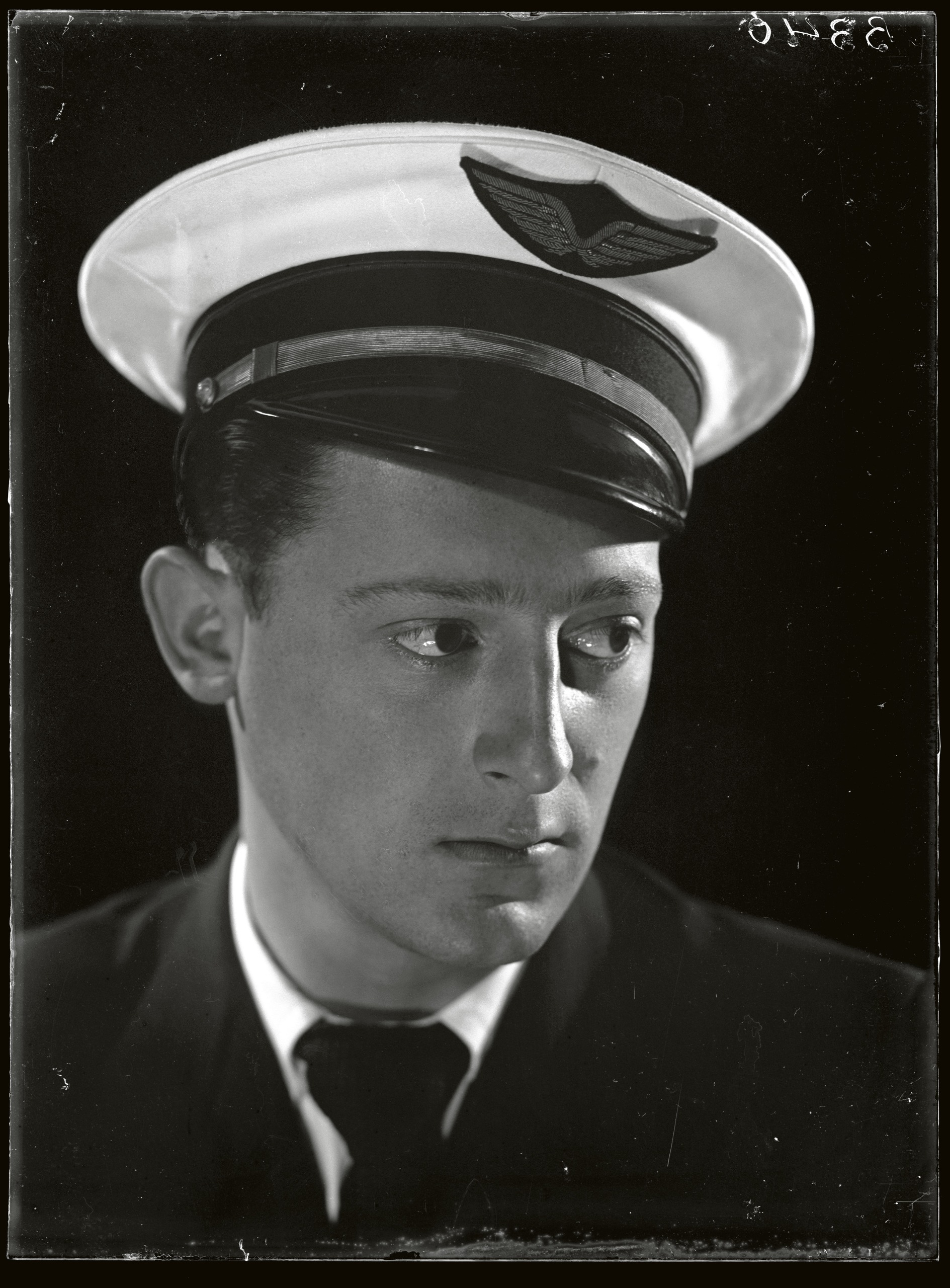 A young man in a peaked naval or aviation cap with a winged emblem looks off to one side in a formal portrait.