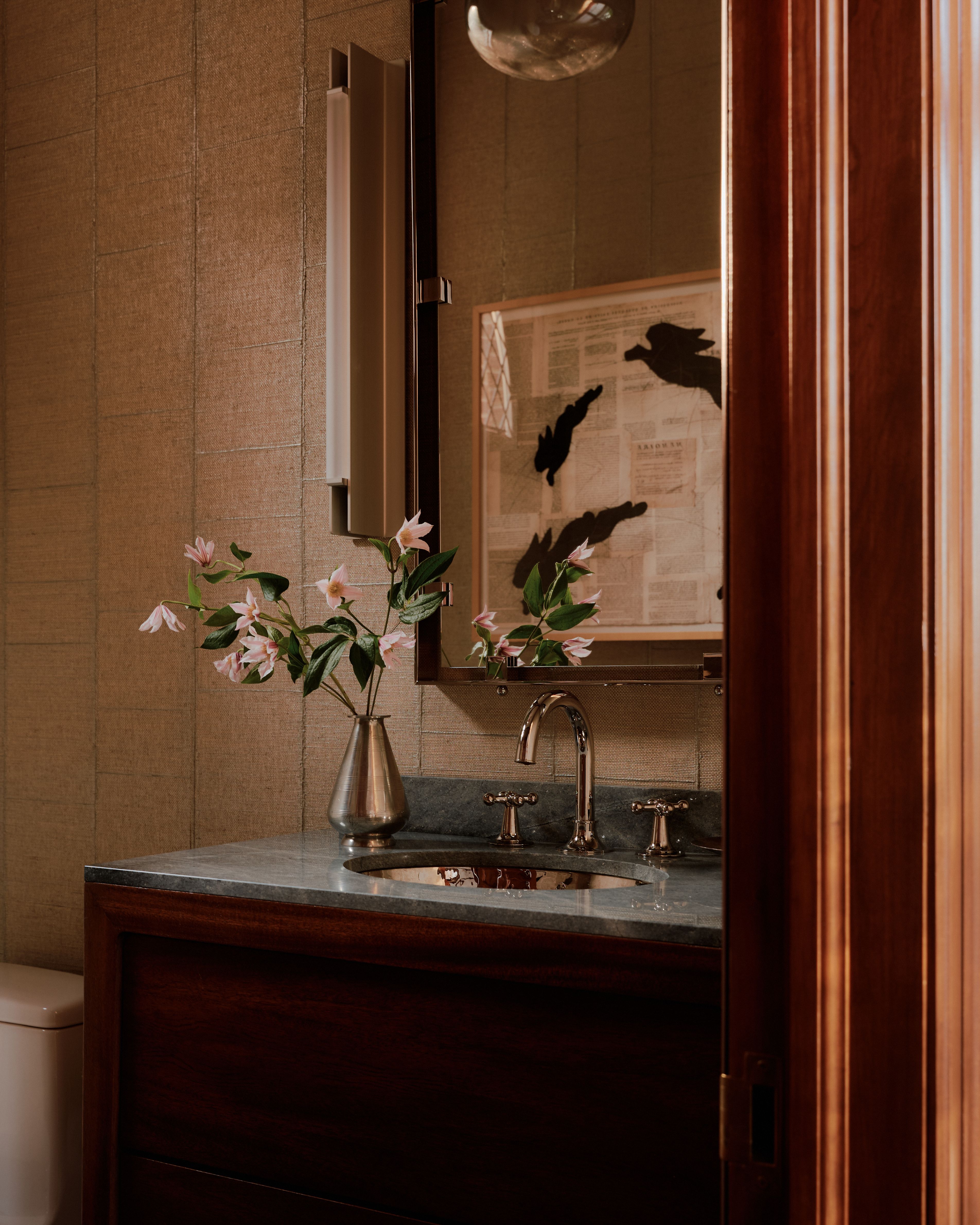 A wood and tile-clad bathroom features a marble-topped basin decorated with matte fixtures and a matching vase of flowers.