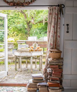 Open french doors leading out to paved garden terrace, with piles of vintage books by the door