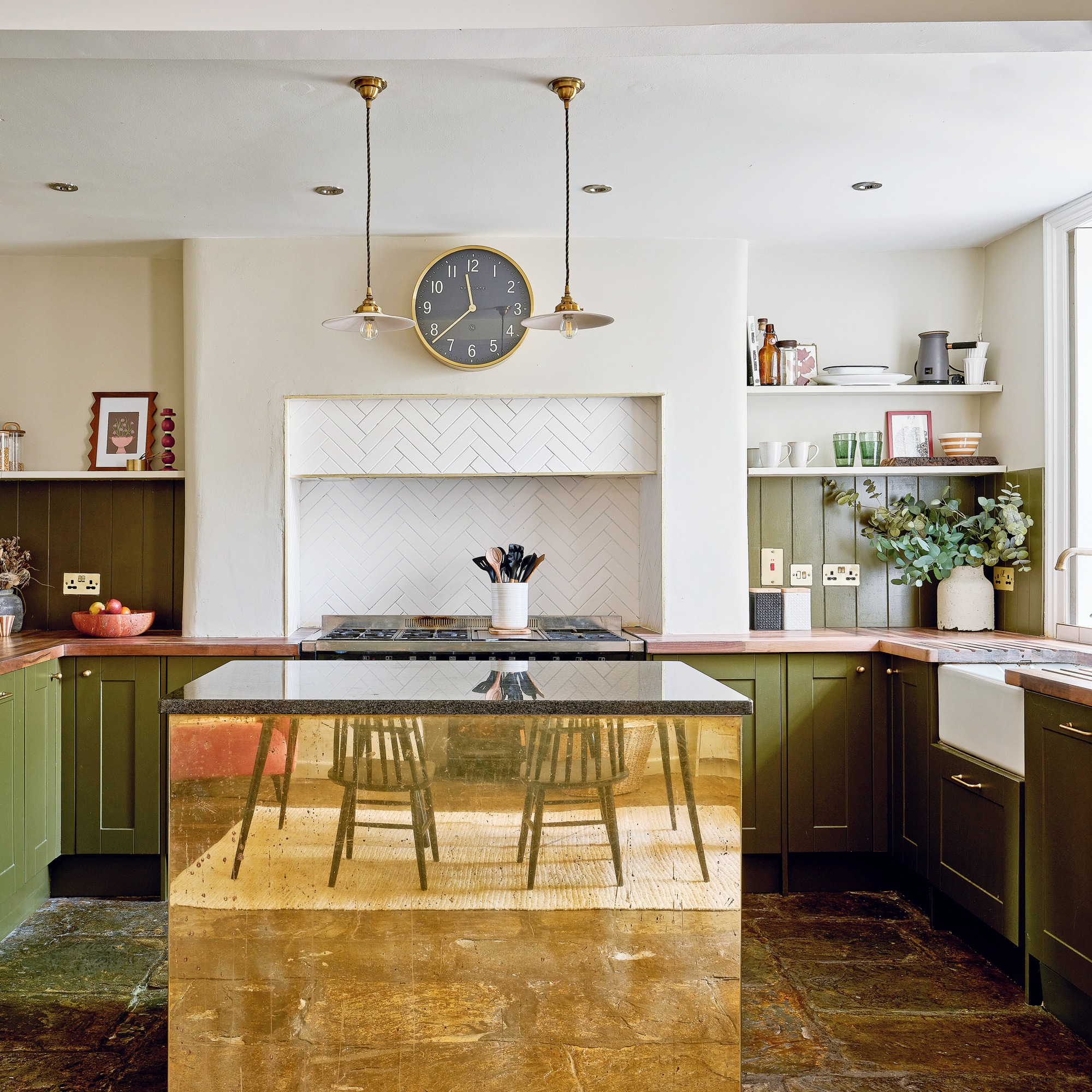 a green and white kitchen with a striking brass fronted kitchen island a Belfast sink, range cooker, white tiled splashback and slate flooring