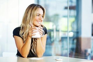 A woman drinks a cup of coffee and looks happy