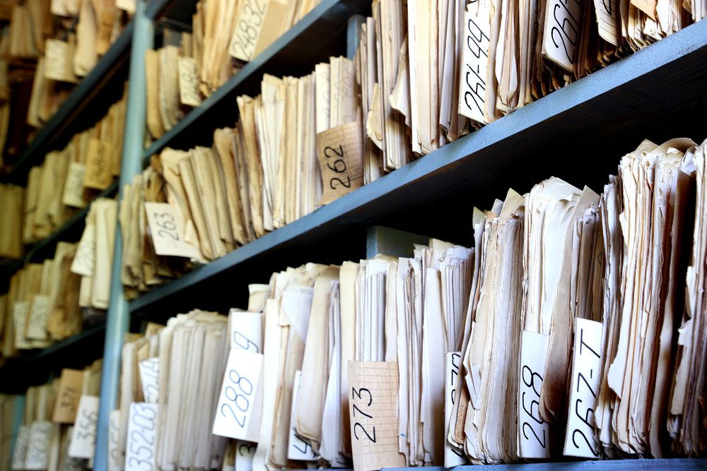 Old paper files in manila folders on shelves in archive.