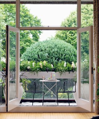 Balcony garden ideas example with small bistro table and chairs looking onto window box planters.