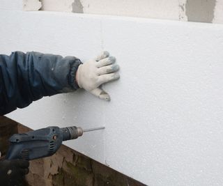 Someone applying foam board insulation to a wall and cutting it to size