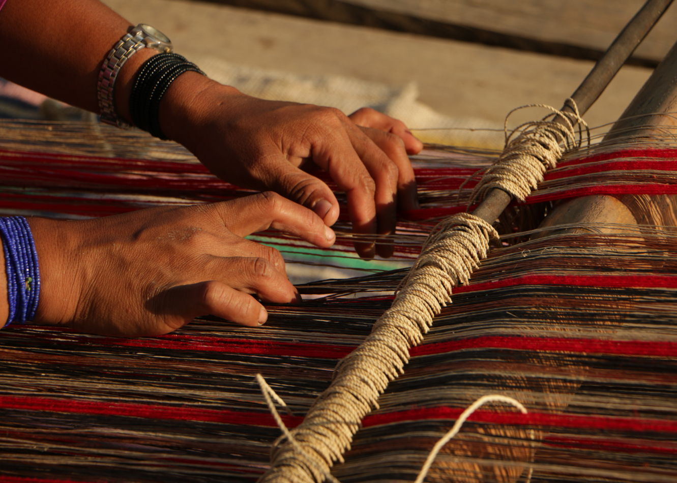 A woman's working photographed while weaving red, brown, and black threads in the sunshine.
