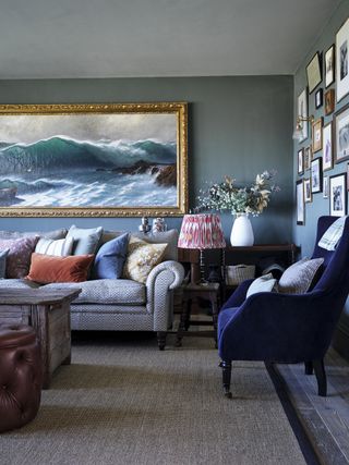 Living room with bluey-grey walls a dark blue velvet chair and a large seascape painting