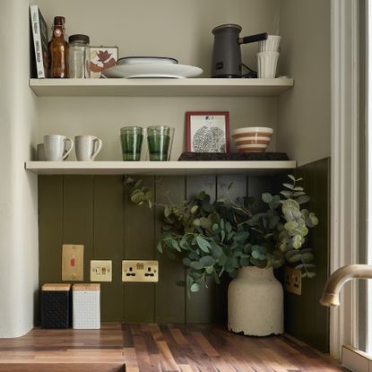 a corner of a kitchen with cream walls, green painted panelling and wood worktops with open shelving