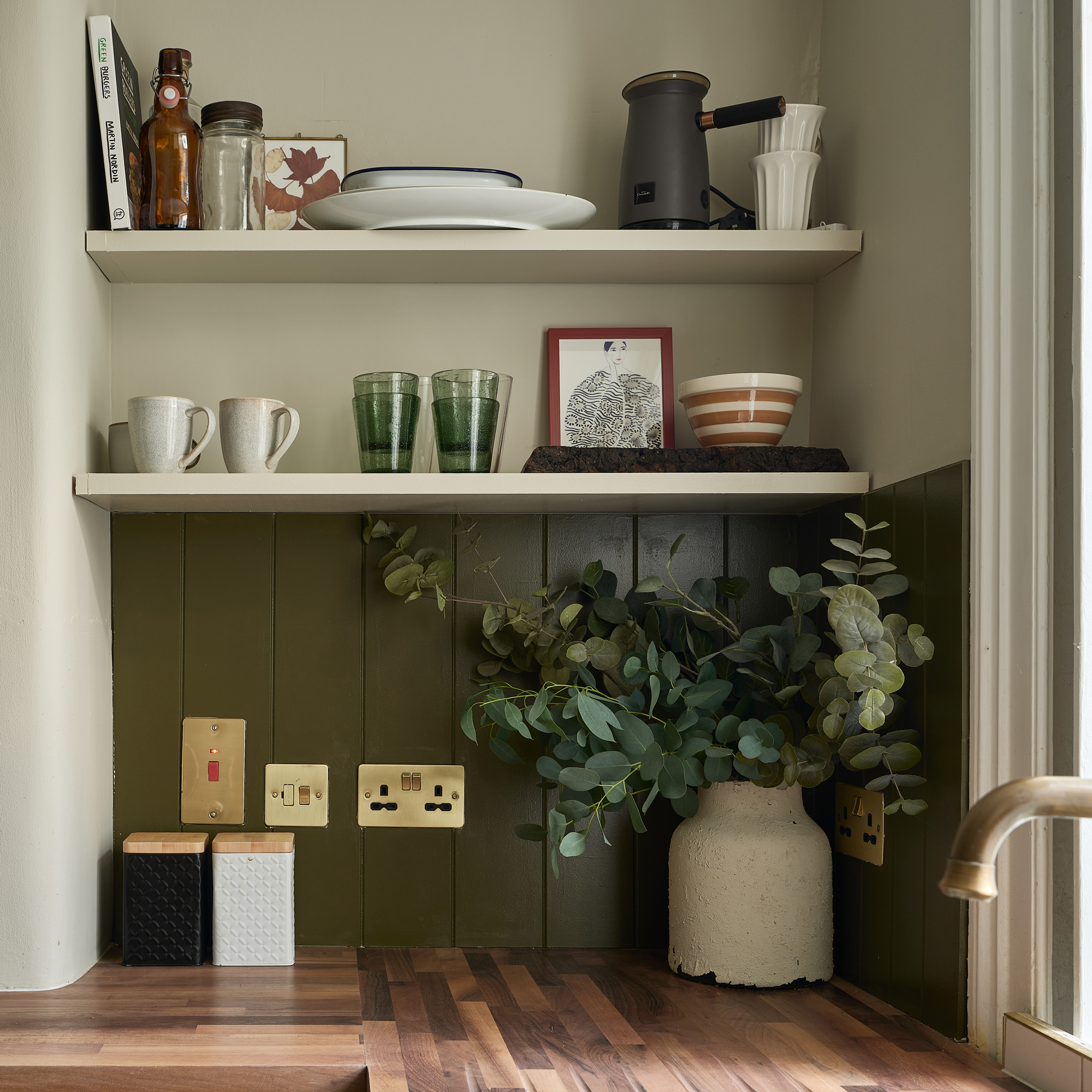 a corner of a kitchen with cream walls, green painted panelling and wood worktops with open shelving