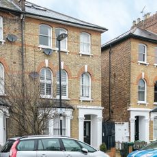 victorian house exterior with bricked wall and white window and cars