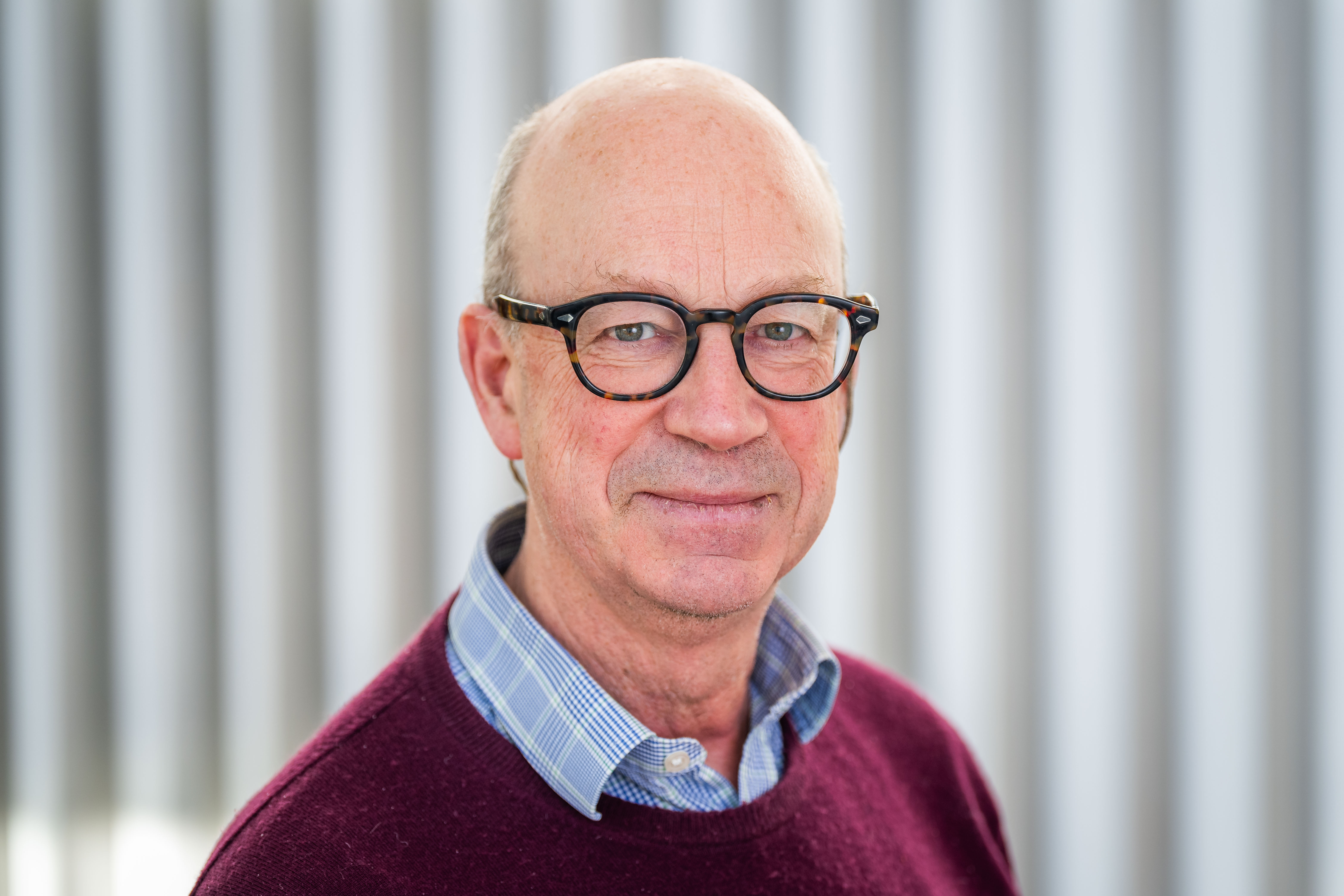 a bald white man with black glasses in a burgundy sweater