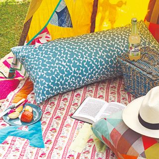 Colourful picnic set up with patchwork blanket, patterned cushions and a tent