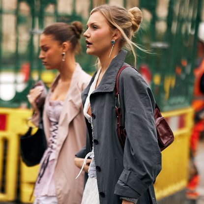 two fashion week attendees wearing high buns and trench coats