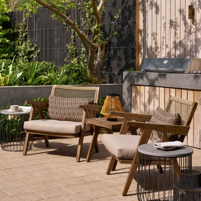A garden with a set of wooden lounge chairs with woven backrests and a matching side table