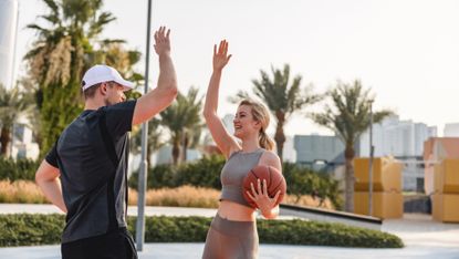 Young woman giving a high-five to a male friend at an outdoor basketball court 