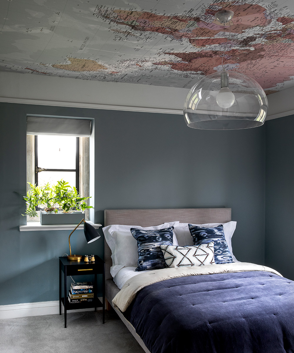 A simple, clear glass ceiling light above a gray bed with blue and white cushions and a blue throw