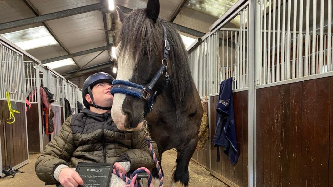 A black horse nuzzling a man in a wheelchair, who looks up at him