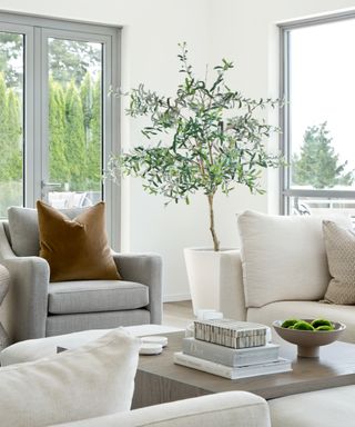 A living room with large windows, white sofa, grey armchair with rust pillow and coffee table