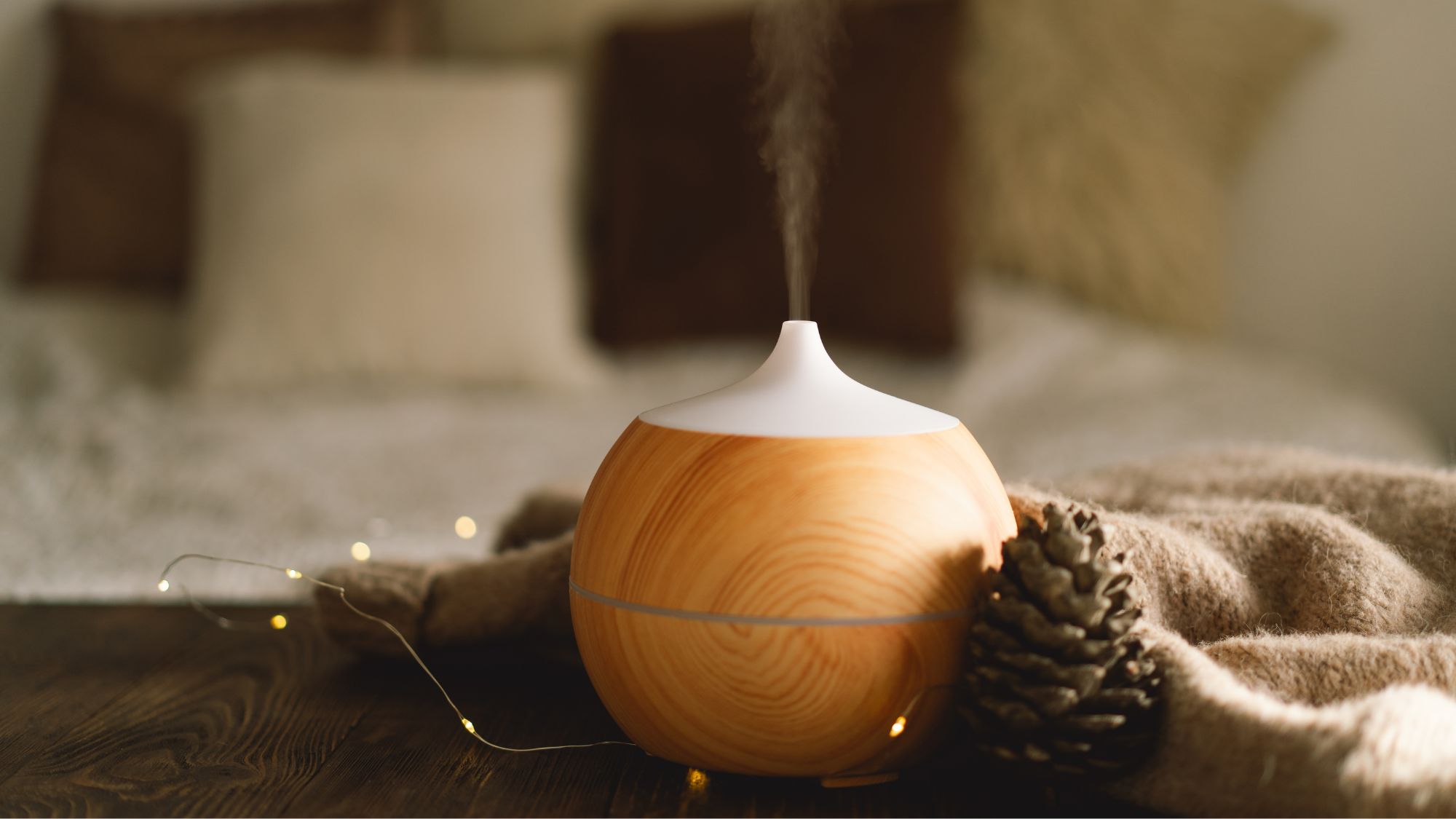image of an electric diffuser on a brown blanket next to fairy lights and a pine cone