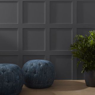 A room with a plant, two seating poufs and a dark gray wall with millwork