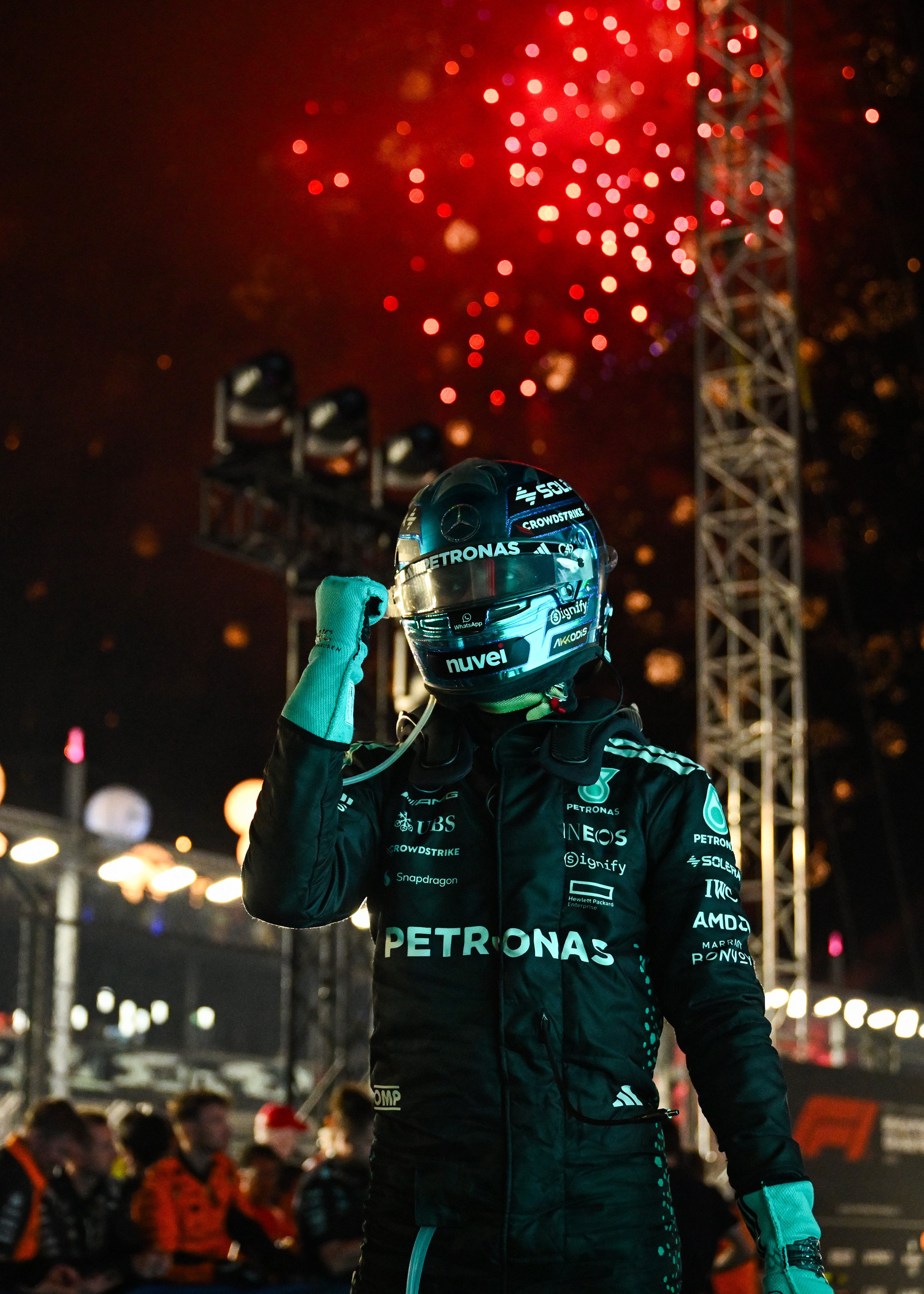 George Russell pumps his fist after winning the Singapore Grand Prix. He&#039;s wearing a black and blue Mercedes race suit, blue helmet and there are fireworks going off behind him