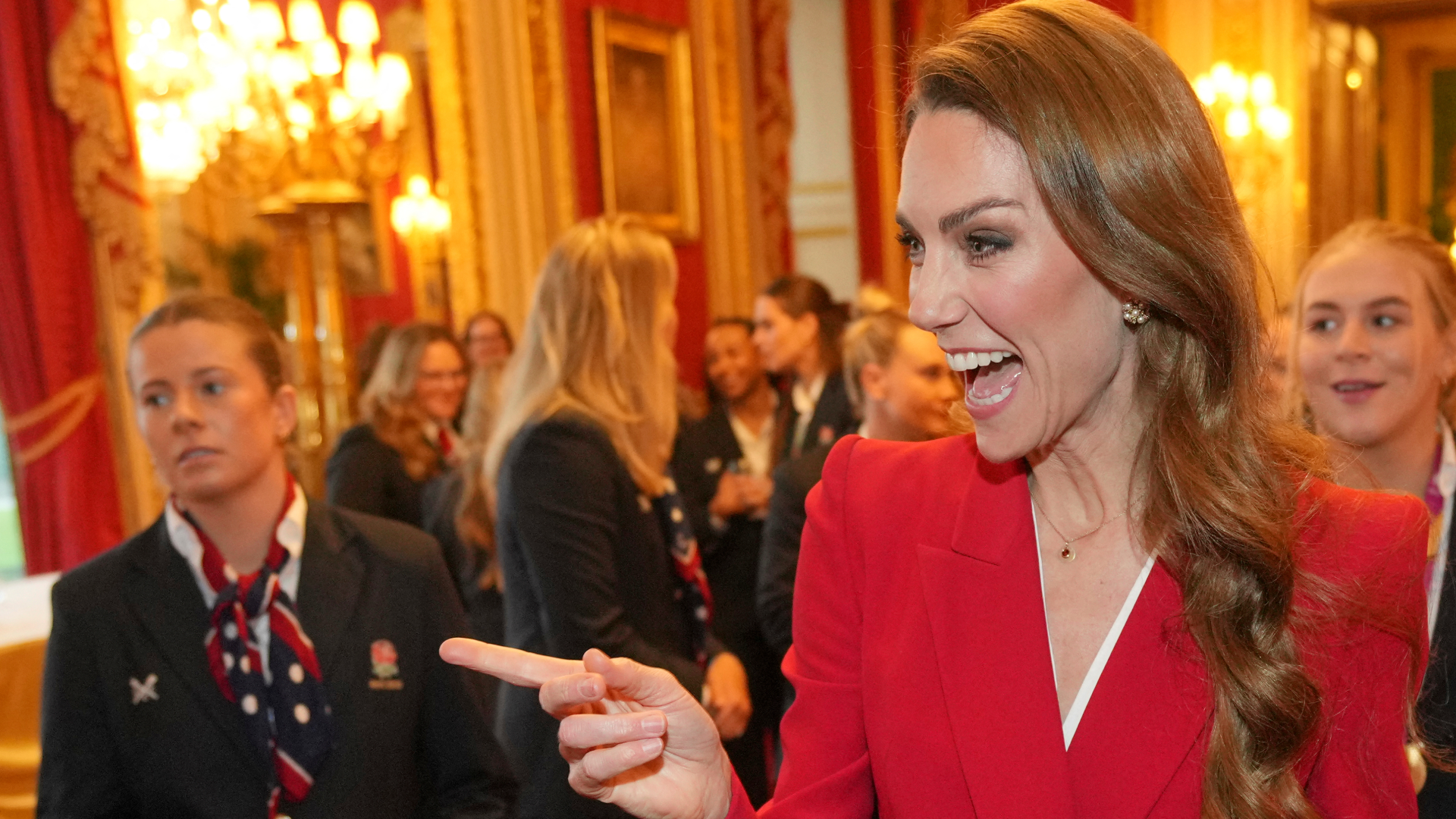 Princess Kate wearing a red blazer, laughing and pointing 