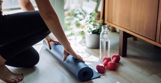 A person rolling out a yoga mat in a house to create an area to relax and recharge