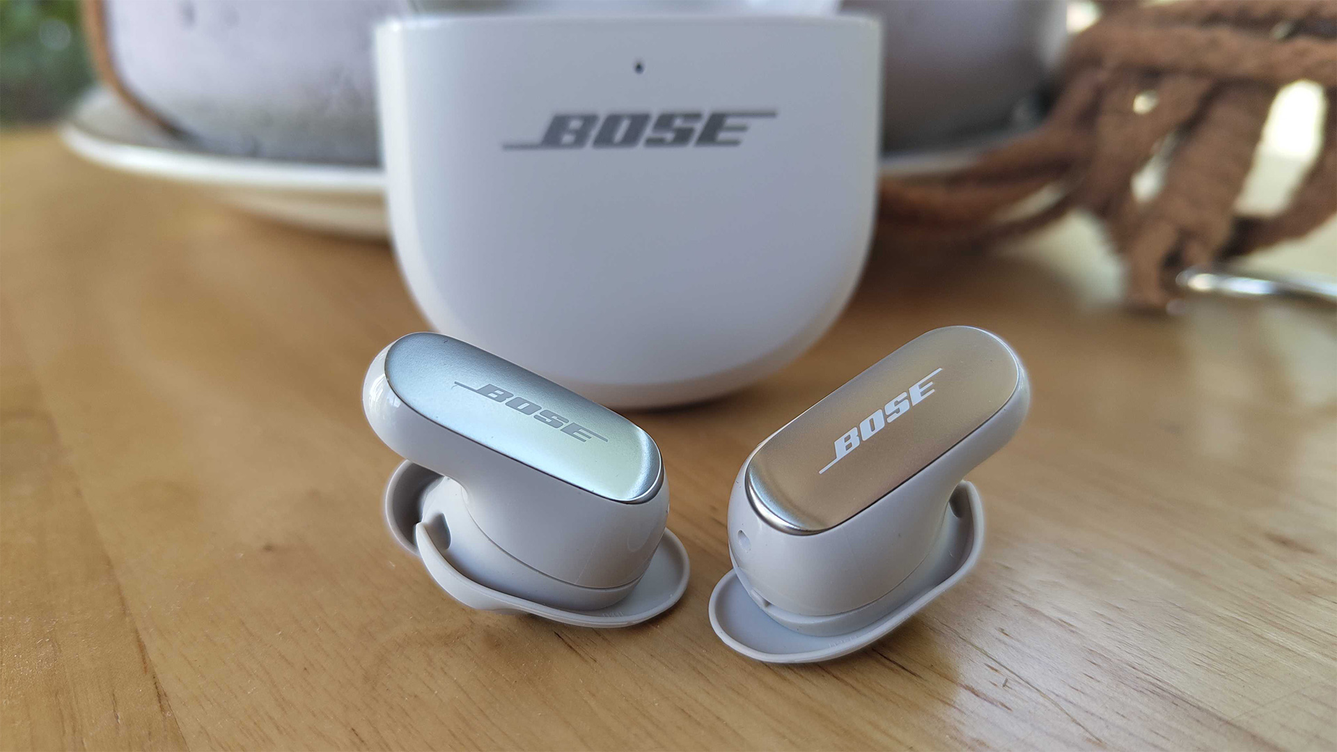 Bose QuietComfort Ultra Earbuds (2nd Gen) wireless earbuds on wooden table in front of charging case