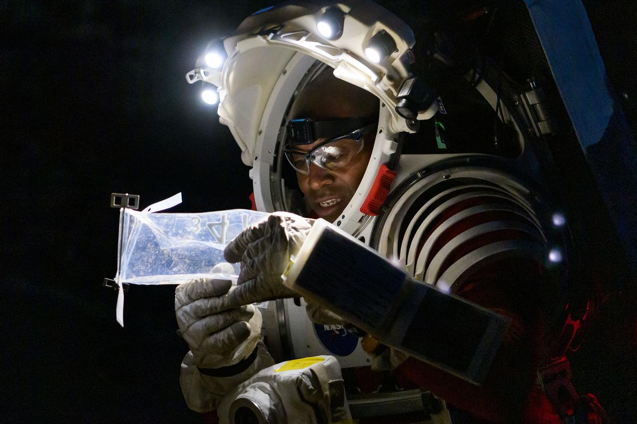 an astronaut in a spacesuit at night. he looks carefully at a plastic bag that contains a sample inside