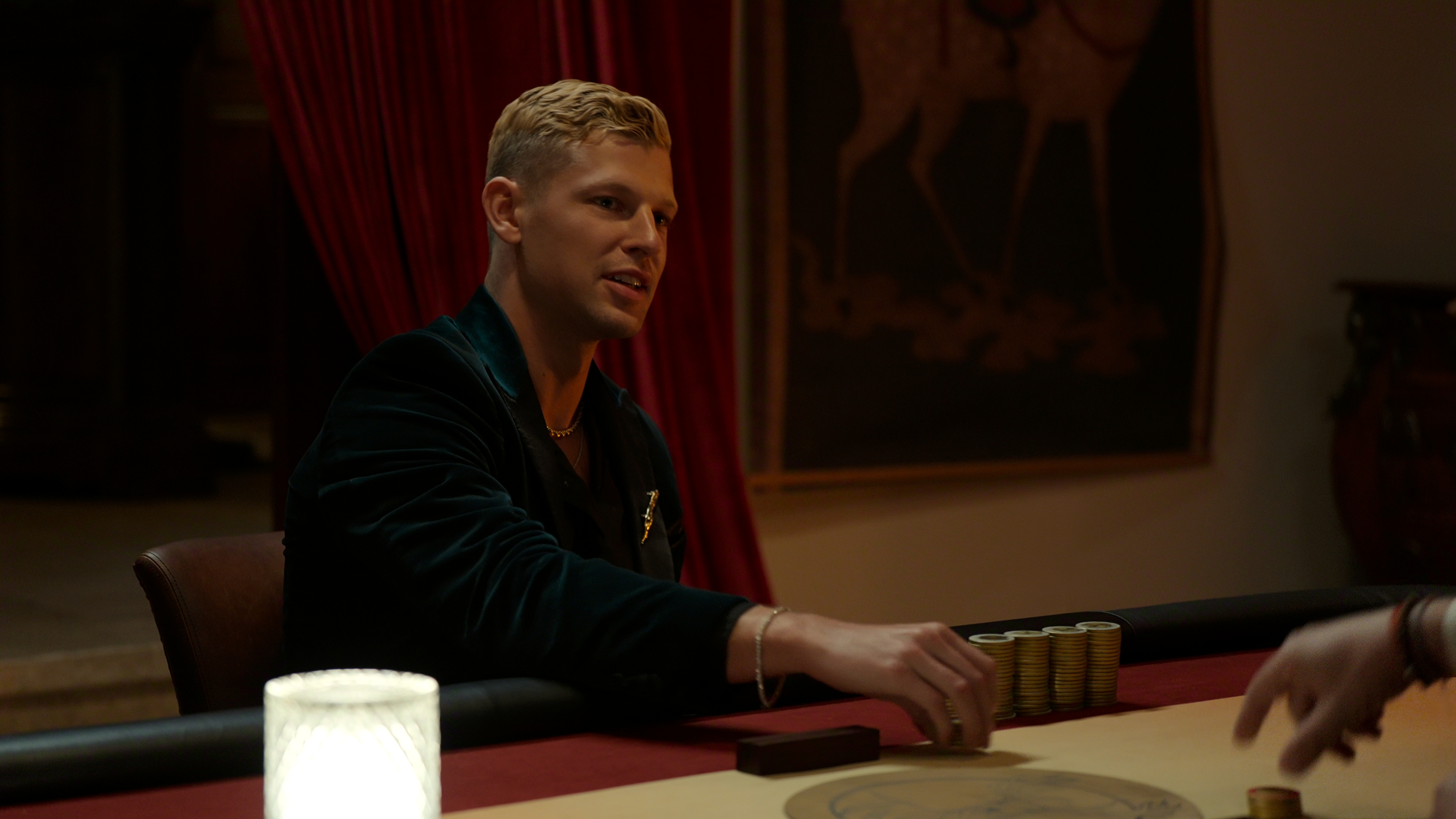 Nick sits in a black suit at a table with stacks of poker chips in front of him.