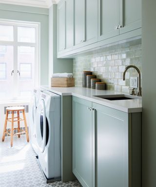 A laundry room with mint green cabinets, glossy tile backsplash and a patterned floor.