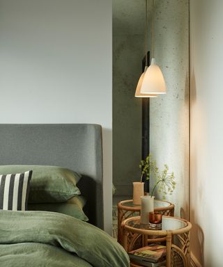 Ambient pendant light hanging above natural bedside in serene bedroom, with mirrored alcove, and mossy green bedlinen and headboard.