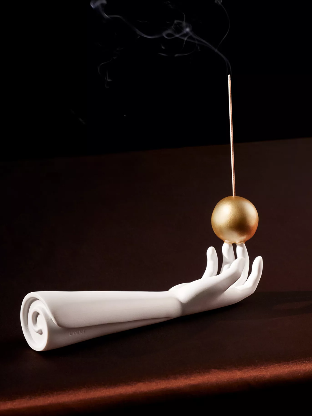A hand shaped incense holder with a gold spherical base from L'Objet
