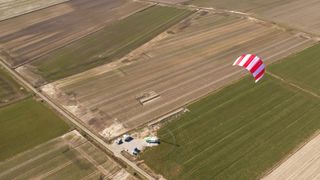 A large red and white kite flying high in the sky, designed to harness the power of high-altitude winds.