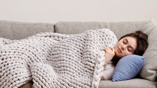 Woman sleeping on the couch with the Bearaby weighted blanket draped over her