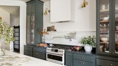 Modern farmhouse style kitchen with marble backsplash, dark green cabinets painted in Sherwin-Williams Pewter Green, and glass-fronted cabinets filled with tableware.
