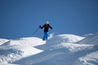 A woman in a black coat and blue pants skiing down a run with moguls