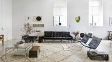 Image of a modern white living room with a black leather sofa and black leather accent chairs. There is a large white rug across the room, and art on the walls.
