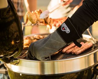 person wearing BBQ gloves cooking on a charcoal grill