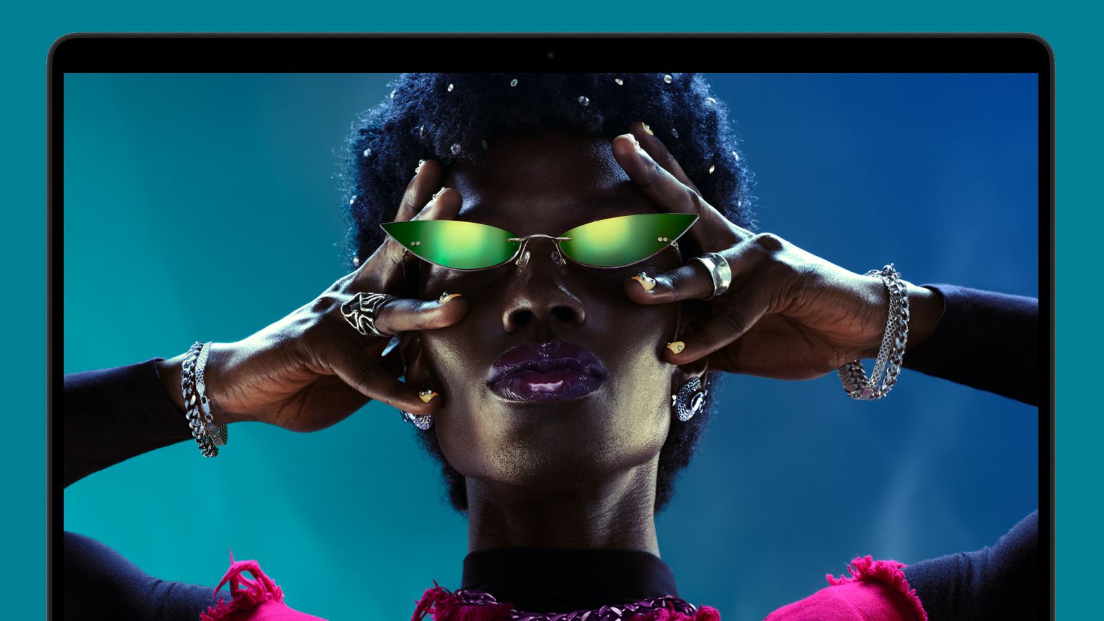 An Apple MacBook Pro M6 on a green background showing the face of a woman wearing sunglasses